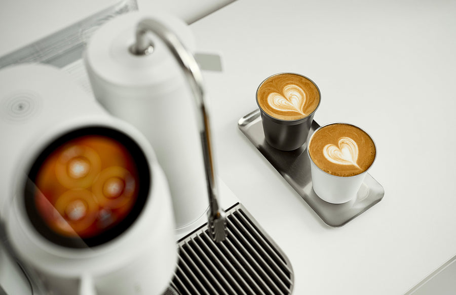 Two cups of coffee with heart-shaped latte art on a metal tray beside a white Meraki espresso machine.
