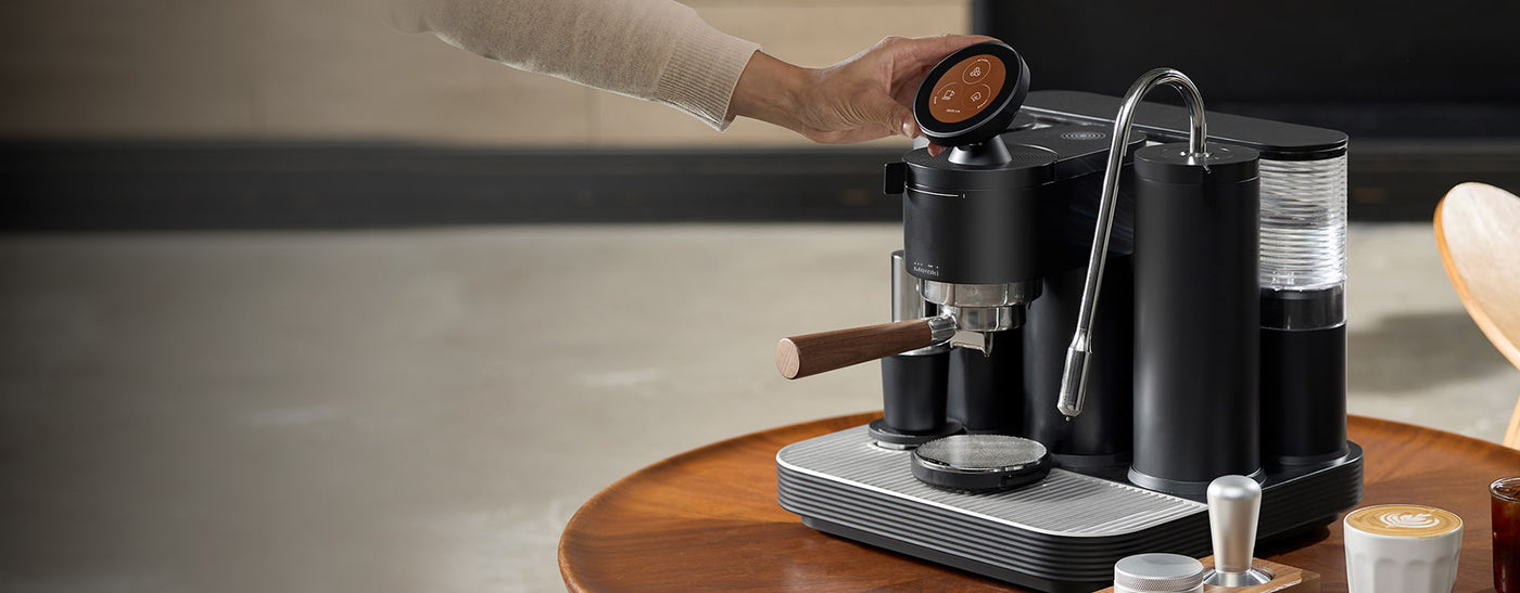 Detailed image of an espresso machine on a table, with a hand adjusting the grinder dial