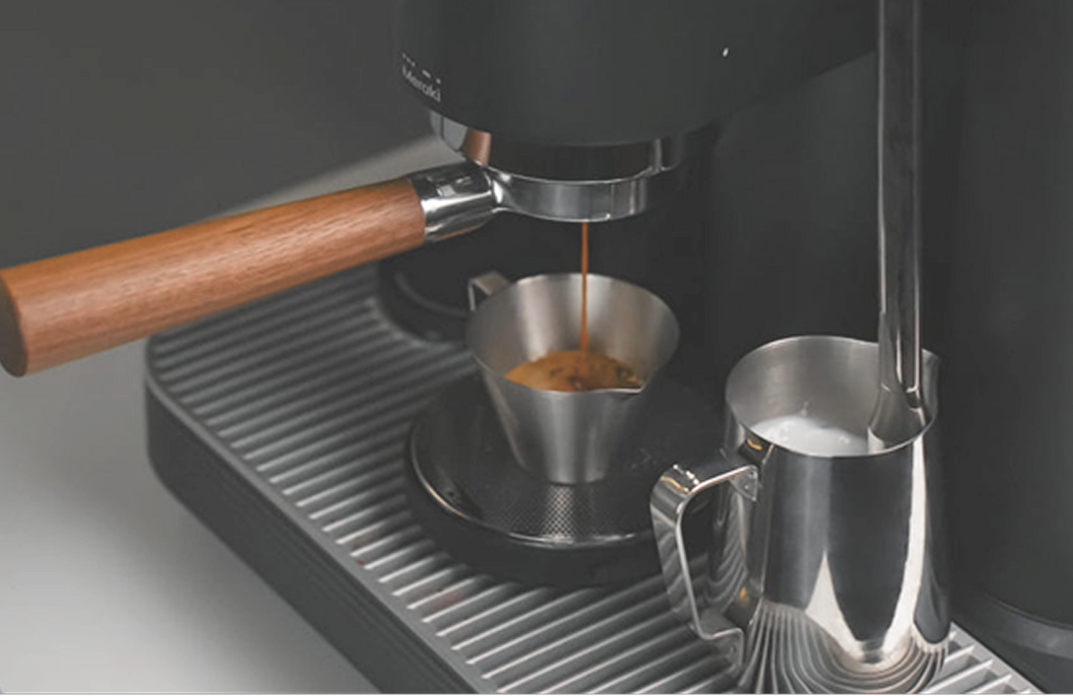 Meraki espresso machine extracting espresso into a stainless steel cup while steaming milk in a pitcher beside it.