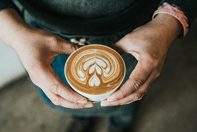 Hands holding a white cup of espresso with intricate latte art, showcasing professional home brewing.
