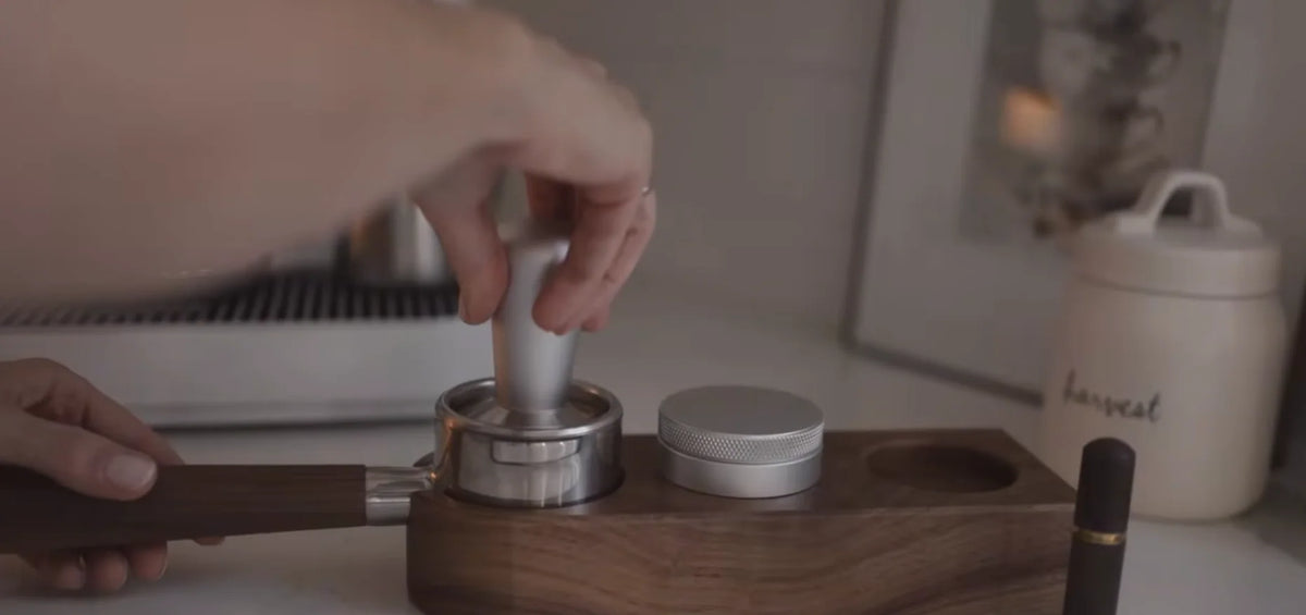 Tamping coffee grounds in a wooden-handled portafilter on a wooden tamping station.