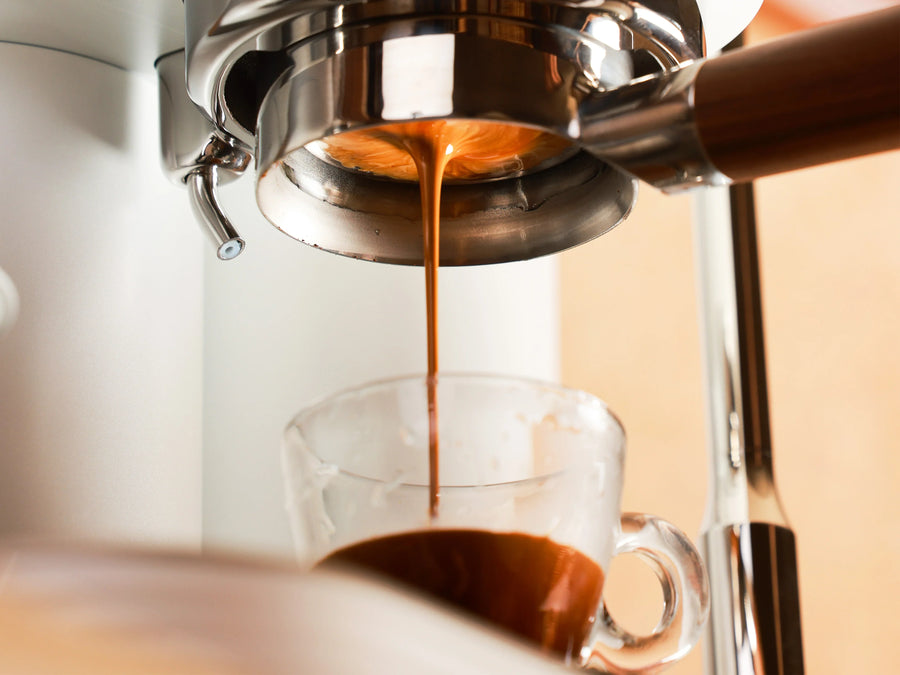 Close-up of espresso flowing from a bottomless portafilter into a clear glass cup.