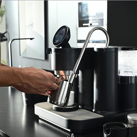 Home barista steaming milk in a stainless steel pitcher with a Meraki espresso machine