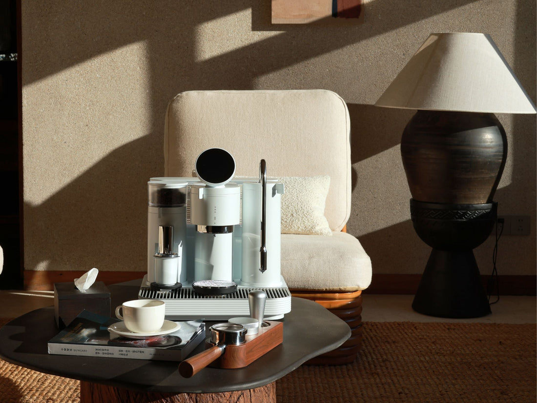 A cozy home scene with a espresso machine, lamp, and vase on a wooden table, creating a warm atmosphere.