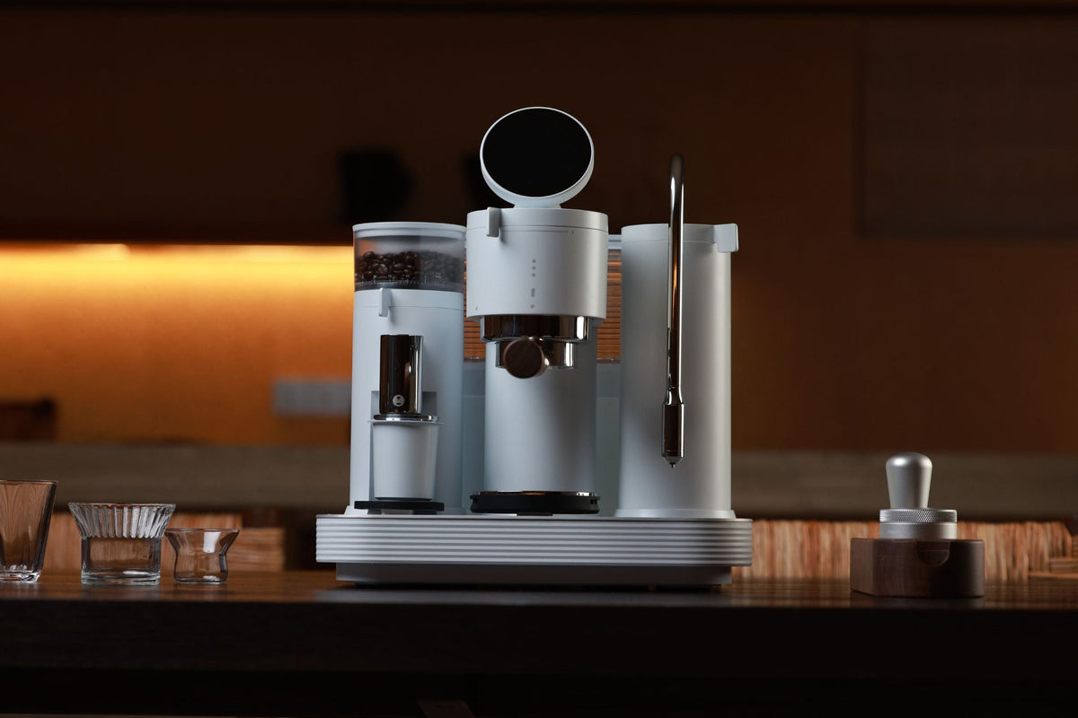 Minimalist white espresso machine with bean hopper and water tank in a dimly lit kitchen.