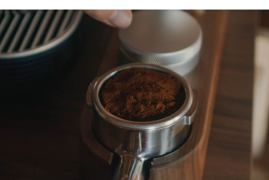 Close-up of a metal portafilter basket filled with dark coffee grounds resting in a wooden tamping station