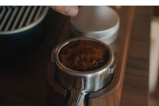 Close-up of a metal portafilter basket filled with dark coffee grounds resting in a wooden tamping station