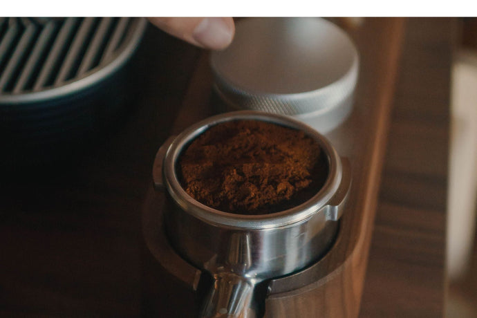 Close-up of a metal portafilter basket filled with dark coffee grounds resting in a wooden tamping station