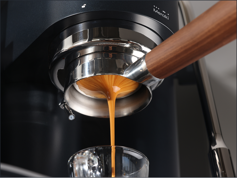 Espresso flowing evenly from a bottomless portafilter on a black Meraki espresso machine.
