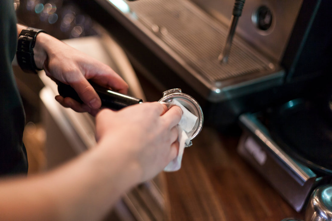 A barista wiping the inside of an espresso portafilter with a white cloth.