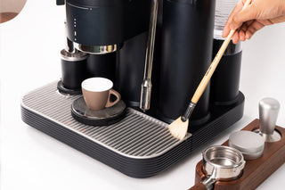 White semi-automatic espresso machine with integrated grinder and steam wand being cleaned on a kitchen counter