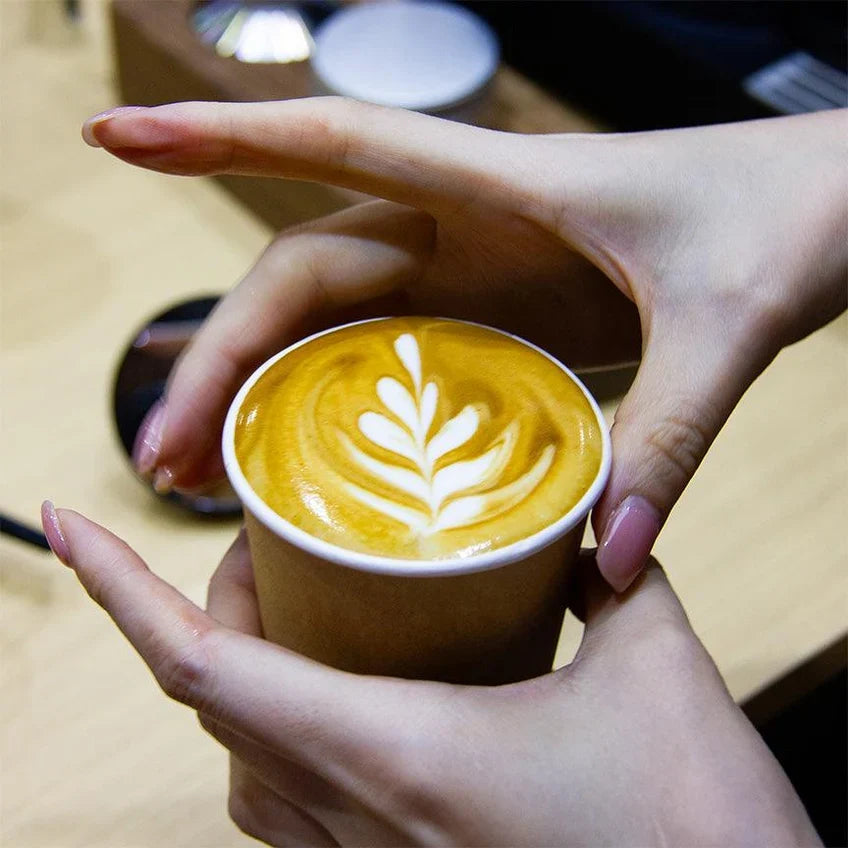 Hands holding a brown cup of coffee topped with leaf-shaped latte art