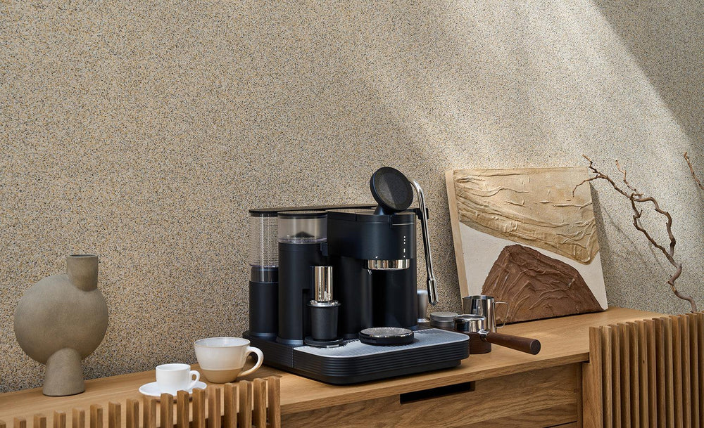 Black Meraki espresso machine on a wooden sideboard with coffee cups, a portafilter, and a milk pitcher