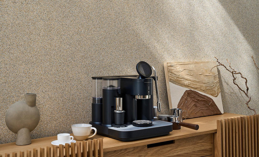 Black Meraki espresso machine on a wooden sideboard with coffee cups, a portafilter, and a milk pitcher