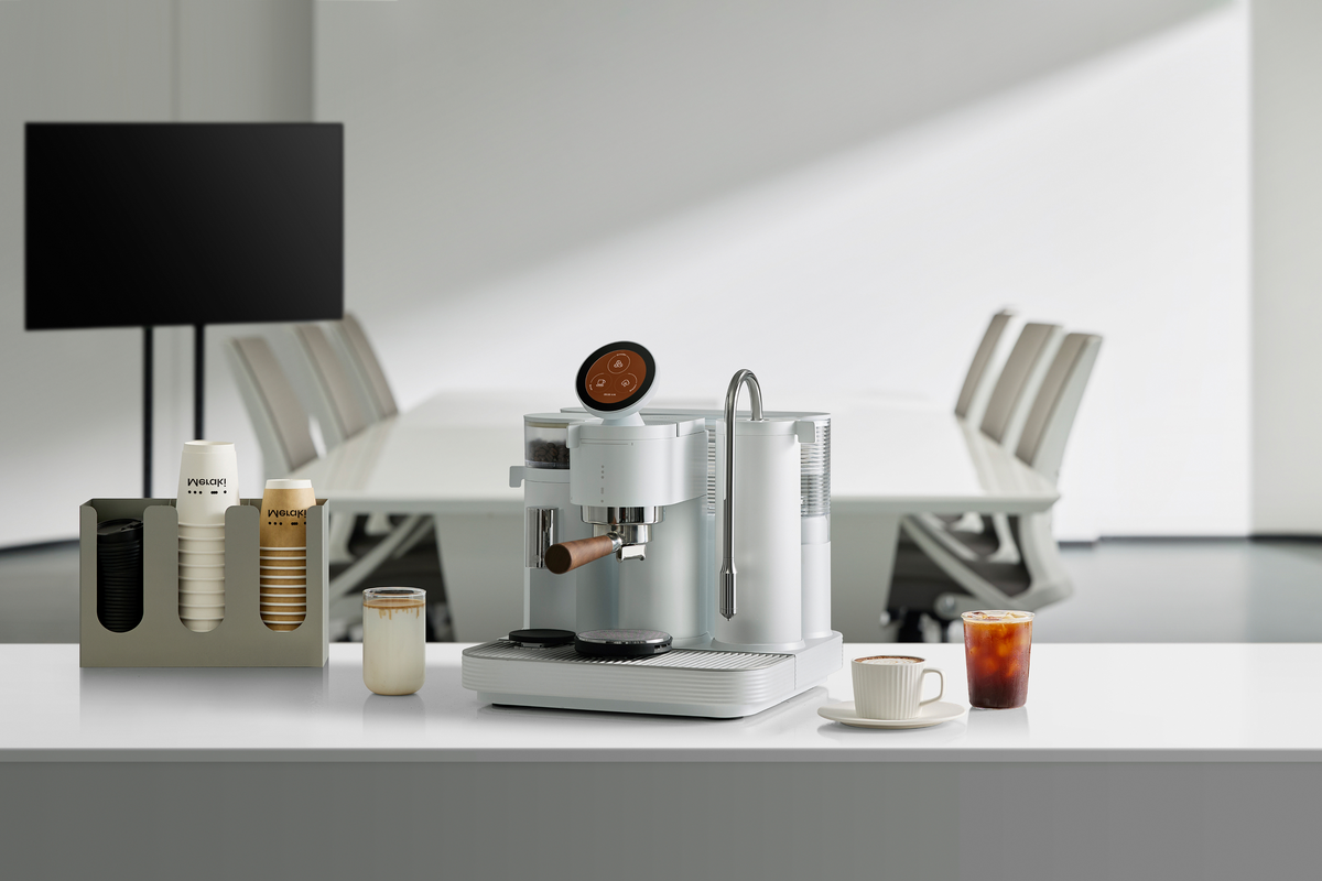 White Meraki espresso machine on an office desk beside a monitor