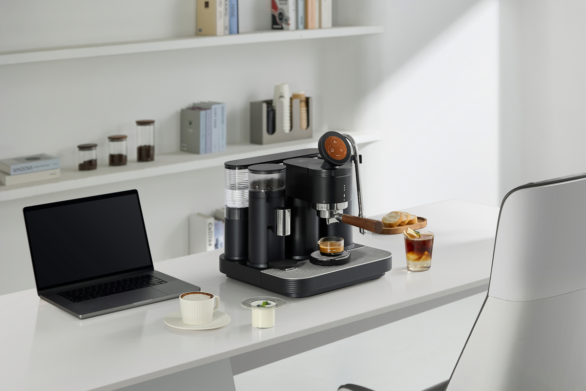 Black Meraki espresso machine on a desk beside a laptop