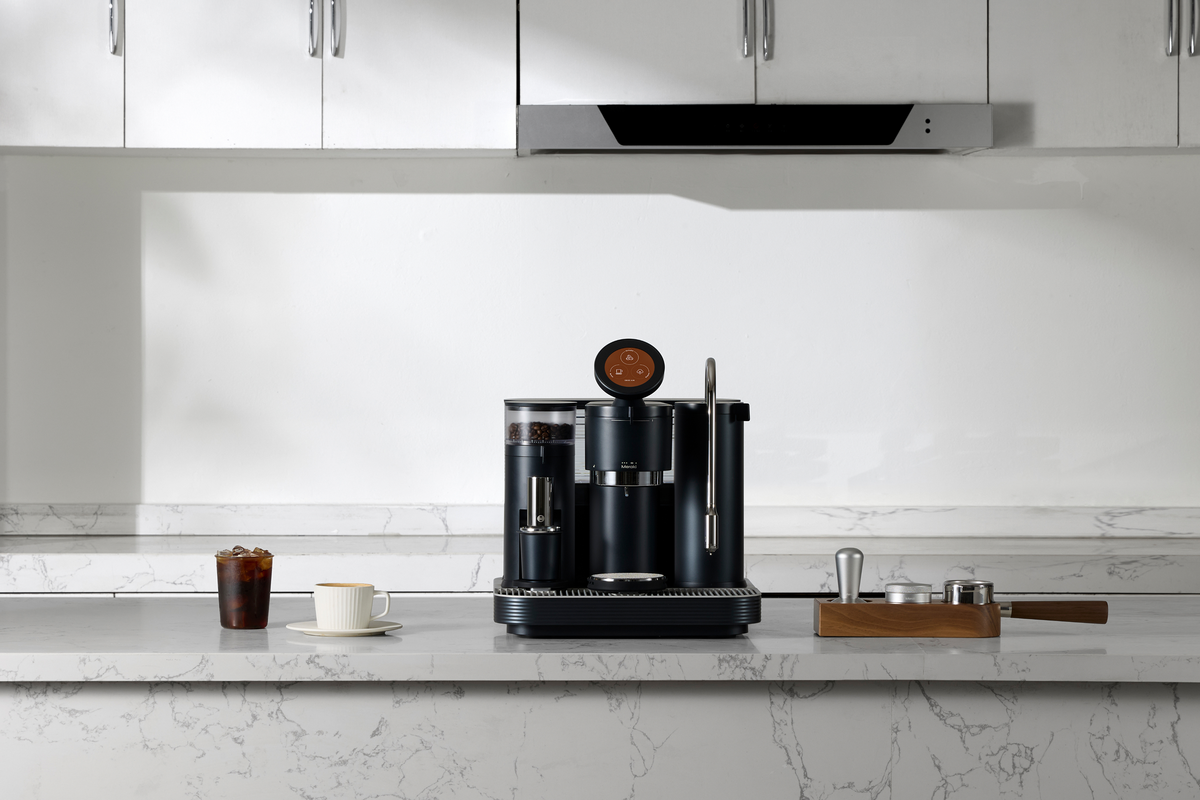 Black Meraki espresso machine on a white kitchen counter beneath a range hood