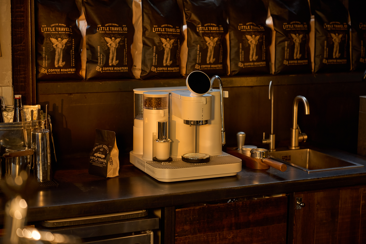 White Meraki espresso machine on a wooden counter below coffee bags