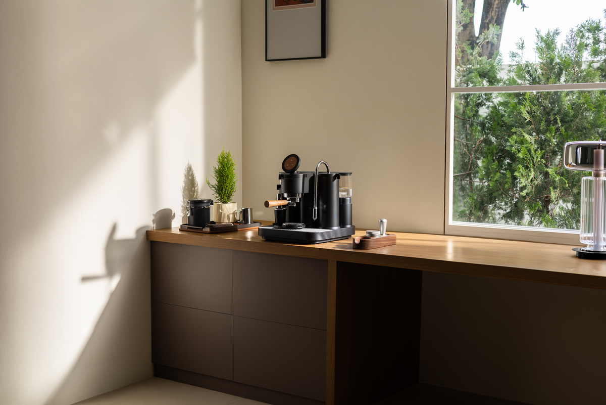 Black Meraki espresso machine on a kitchen counter beside a window