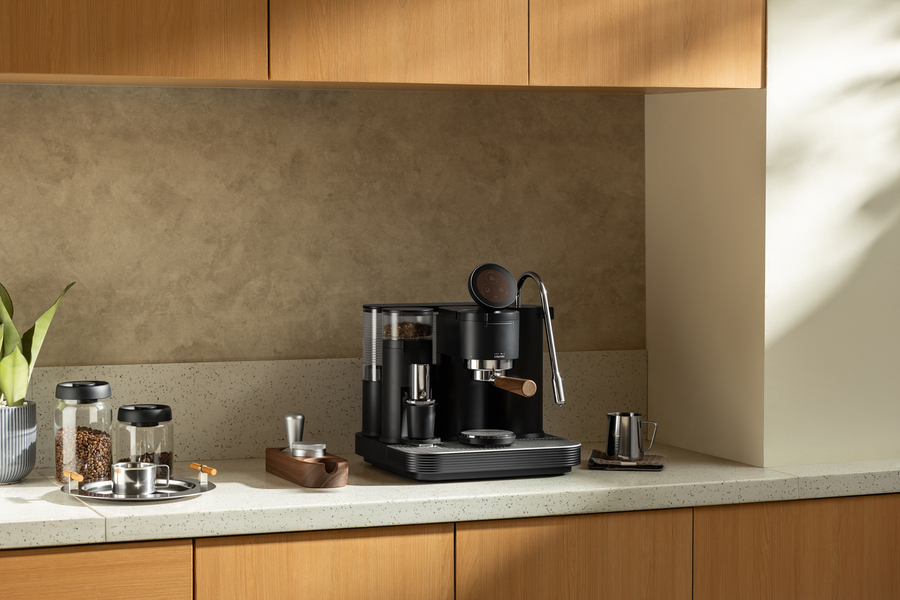 Black Meraki espresso machine on a counter beneath kitchen shelving