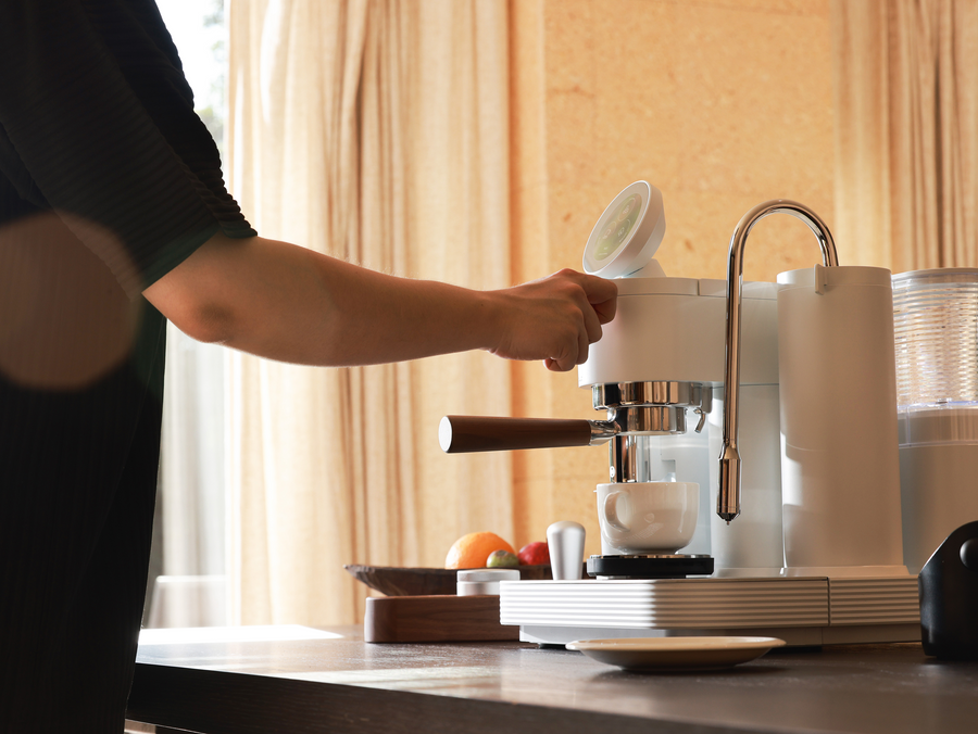 Preparing coffee with a white Meraki espresso machine beside curtains