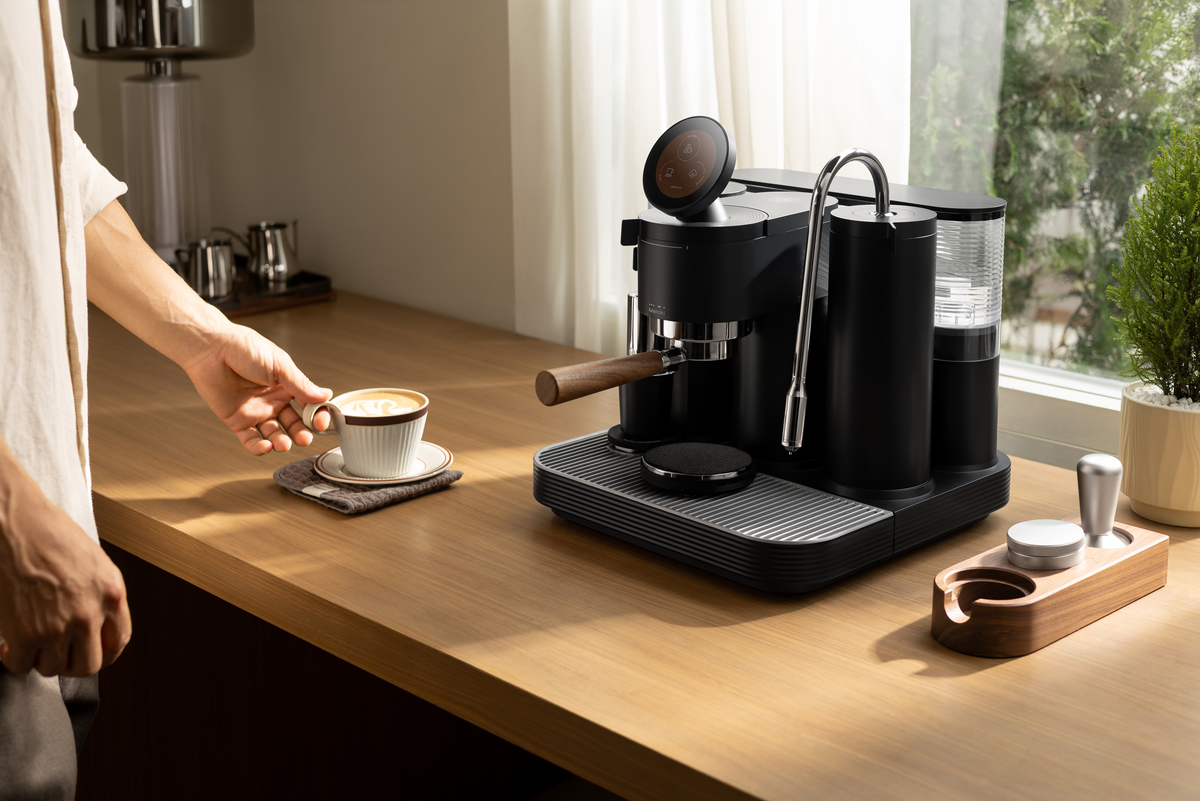 Holding a coffee cup beside a black Meraki espresso machine