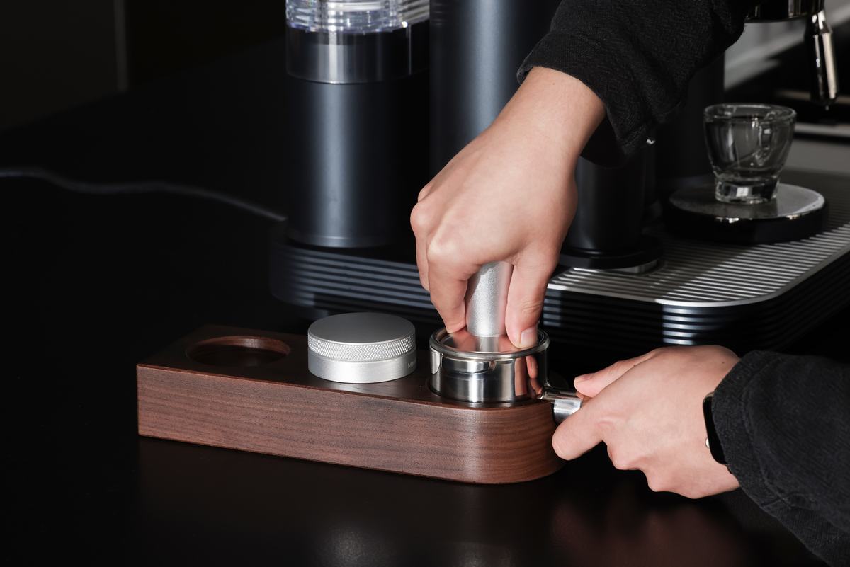 Tamping coffee in a portafilter on a preparation station beside a Meraki machine