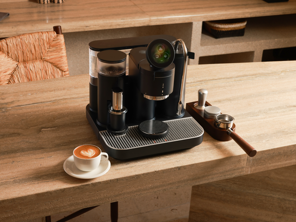 Black Meraki espresso machine with a latte and portafilter on a wooden counter