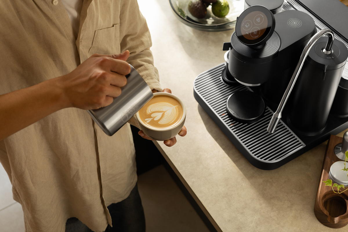 Pouring latte art into a white cup beside a black Meraki espresso machine