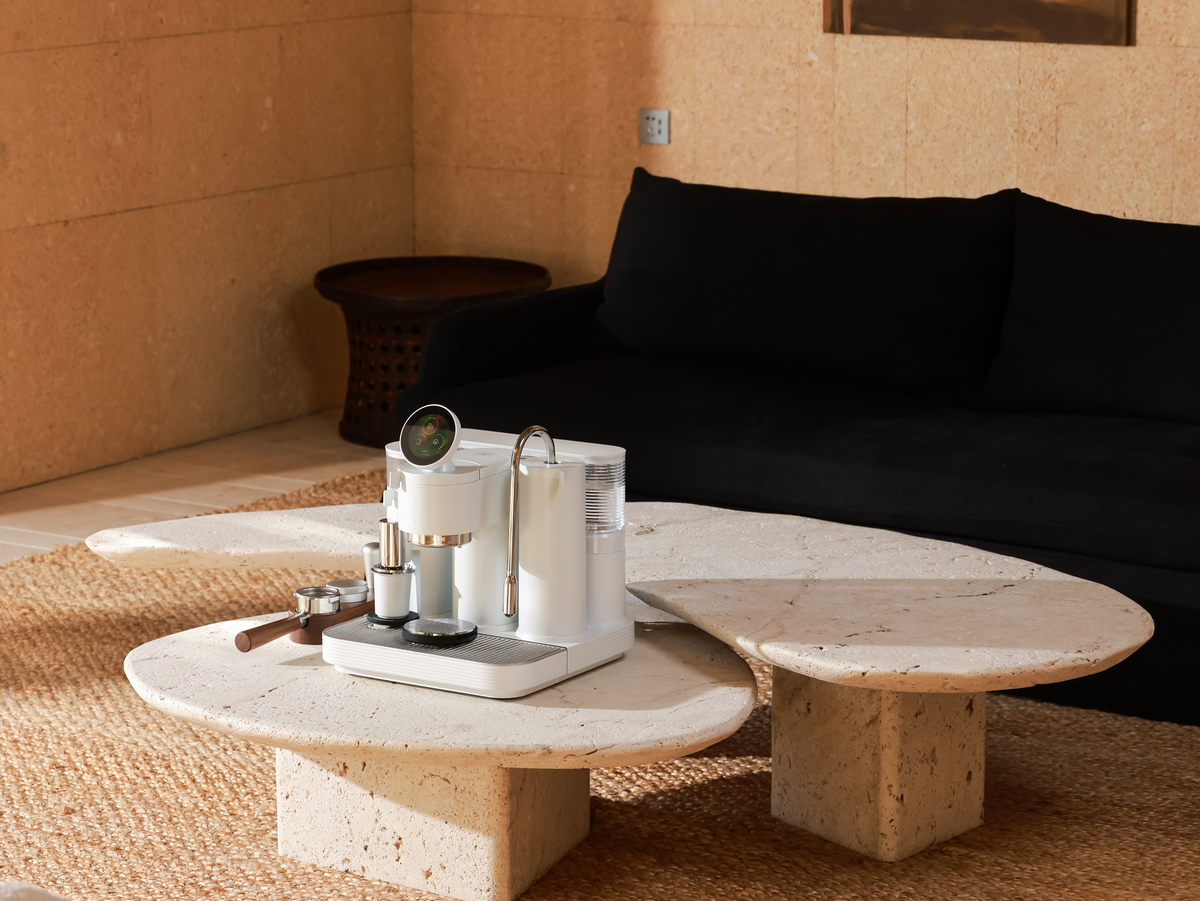 White Meraki espresso machine on a round table beside a sofa