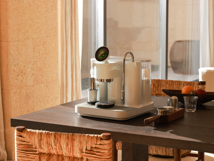 White Meraki espresso machine on a wooden counter beside curtains