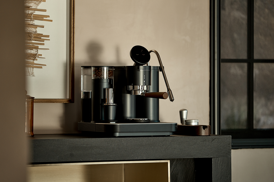 Black Meraki espresso machine on a counter in a dark green kitchen