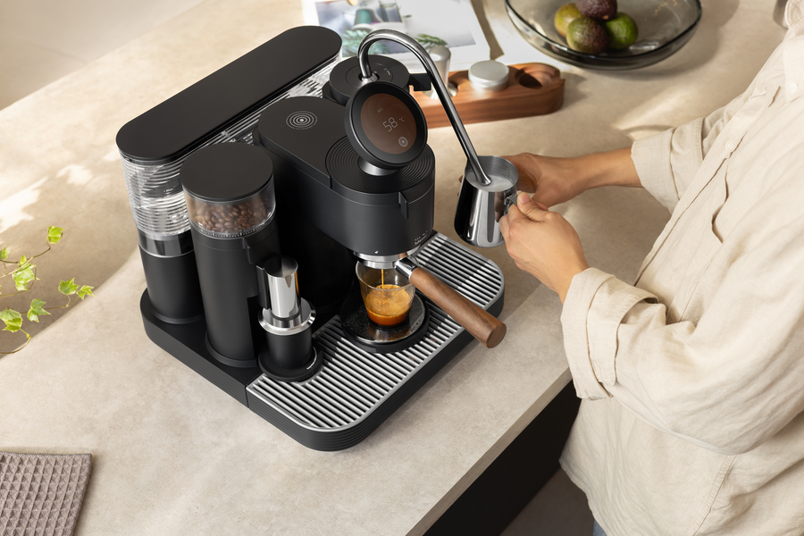 Preparing coffee with a black Meraki espresso machine, cup and milk pitcher